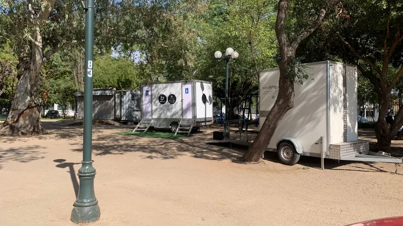 Dos tráileres de baños móviles Maihue instalados entre eucaliptos en un parque, para eventos que necesitan más de una unidad