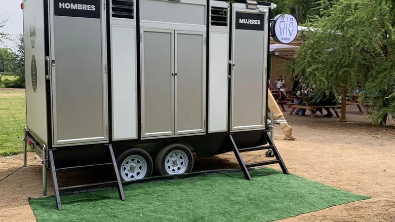 Tráiler de baños móviles premium Maihue sobre césped en un evento al aire libre, junto al toldo y las mesas de los invitados