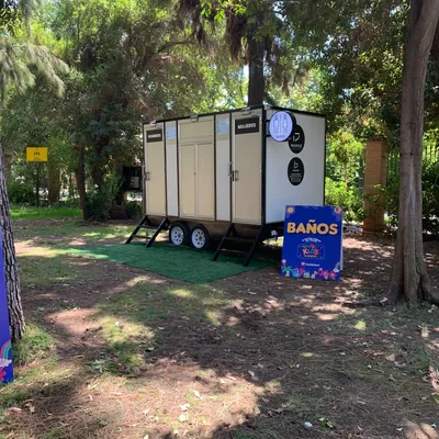 Tráiler de baños móviles Maihue en un parque durante una fiesta infantil, con señalética de baños