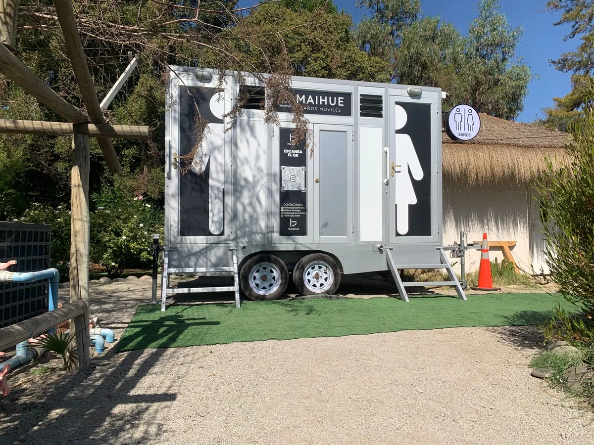 Tráiler de baños premium Maihue instalado junto a un quincho con techo de paja en una parcela, listo para una fiesta privada